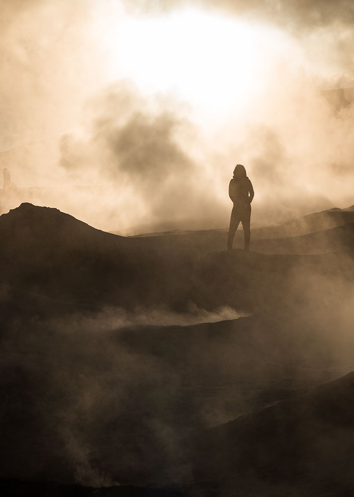 Figure standing amongst steam at the Sol de Mañana Geyser at dawn, Reserva Eduardo Avaroa, Bolivia